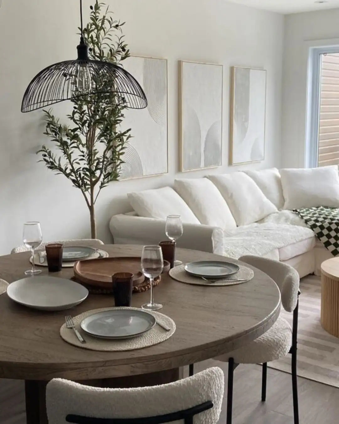 Round wooden dining table with a natural finish and set for four, featuring light gray plates on woven placemats.