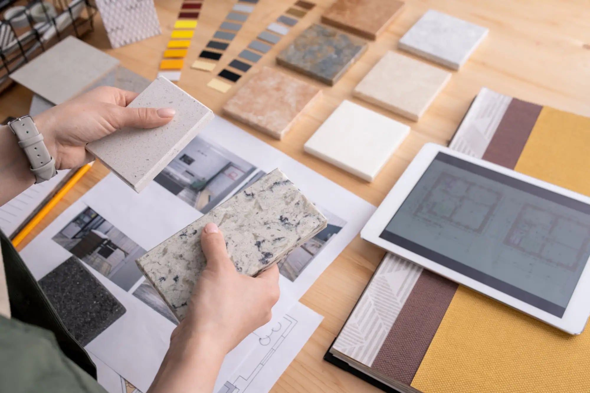 Hands holding two rectangular samples of textured, speckled stone-like material in neutral tones.