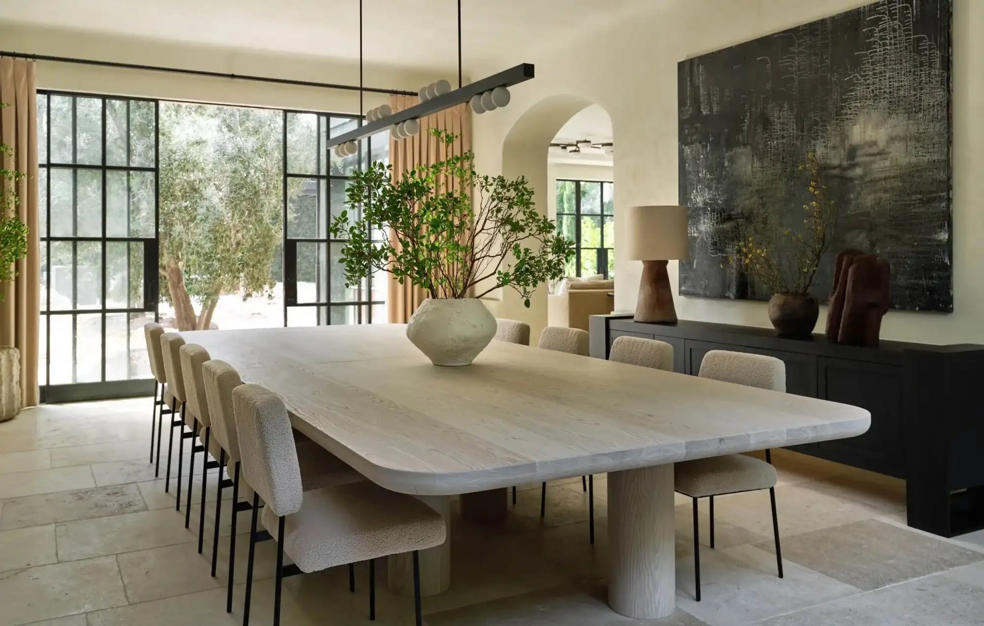 Light-colored wooden dining table with a smooth, minimalist surface and integrated stone-like pedestal legs.